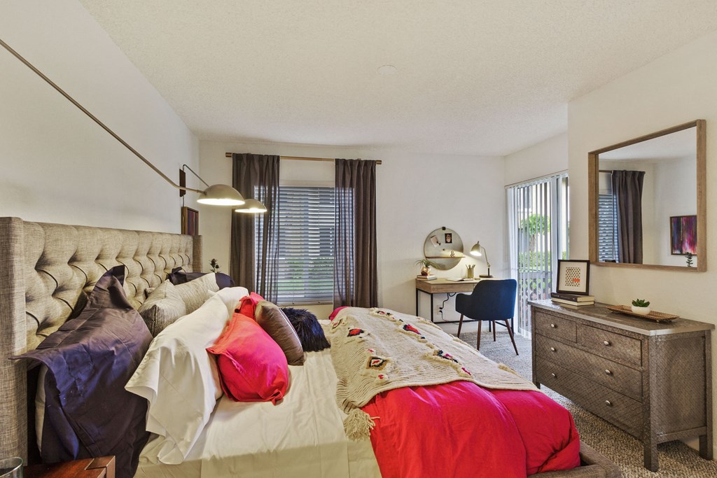 A bedroom with a large bed, a desk with a chair, and a mirror on the wall.